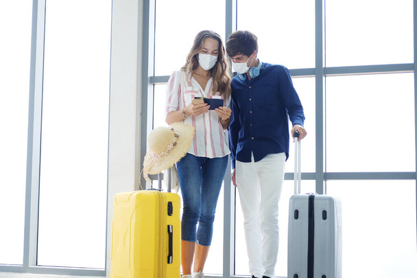 Νεαρό Καυκάσιος ταξιδιώτης ζευγάρι αγαπούν φορούν μάσκα για την πρόληψη για τον ιό covid-19 κατέχει διαβατήριο και τον έλεγχο κάρτα επιβίβασης μαζί στο αεροδρόμιο. Healthcare για ταξίδι του μέλιτος στις διακοπές. - Φωτογραφία, εικόνα