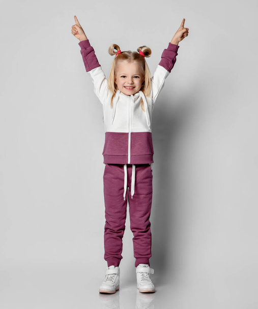 Smiling little girl raised her hands up on a gray background. - Foto, afbeelding