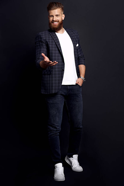 Confident and handsome. Full length of young man with ginger beard in smart-casual clothes smiling looking at camera while posing against black background. - Foto, imagen
