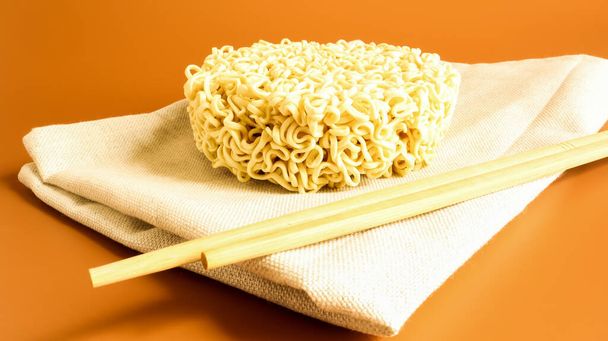 raw instant noodles on a towel with chopsticks on a yellow background. pasta, for the preparation of which it is enough to pour boiling water over it and wait a few minutes. Copy space - Photo, Image