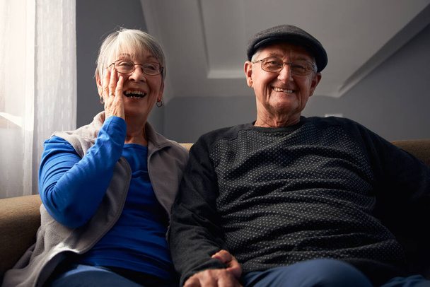 Uśmiechnięta para seniorów siedząca na kanapie w domu oglądająca razem telewizję - Zdjęcie, obraz