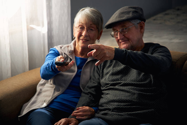 Liebendes Senioren-Paar sitzt zu Hause auf Sofa und schaut gemeinsam fern - Foto, Bild