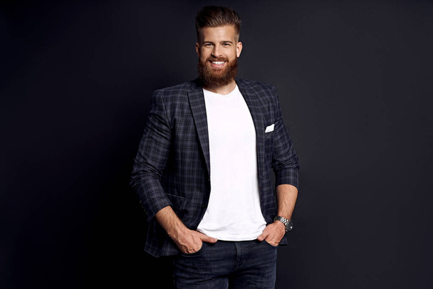 Confident and handsome. Young man with ginger beard in smart-casual clothes smiling looking at camera while posing against black background. - Фото, изображение