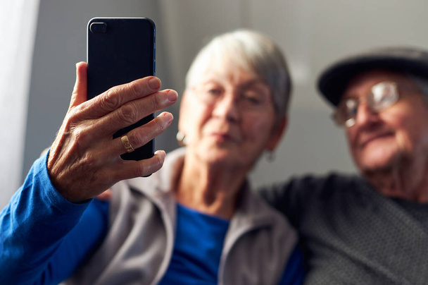 Evde oturan yaşlı çift cep telefonuyla ailelerine video araması yapıyor. - Fotoğraf, Görsel