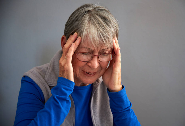 Старшая женщина страдает от стресса или головной боли в доме, держа голову в боли - Фото, изображение
