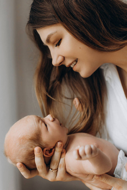 Overjoyed young woman hold newborn baby girl in arms, caring mother looking with love at the little daughter, smiling, enjoy happiness of parenting, maternity concept - Foto, Imagem