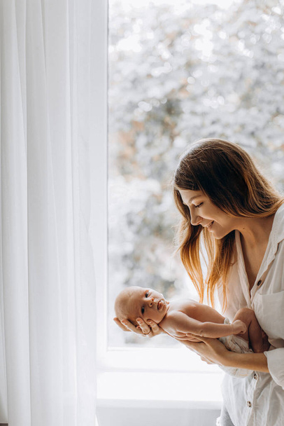 Overjoyed young woman hold newborn baby girl in arms, caring mother looking with love at the little daughter, smiling, enjoy happiness of parenting, maternity concept - Zdjęcie, obraz