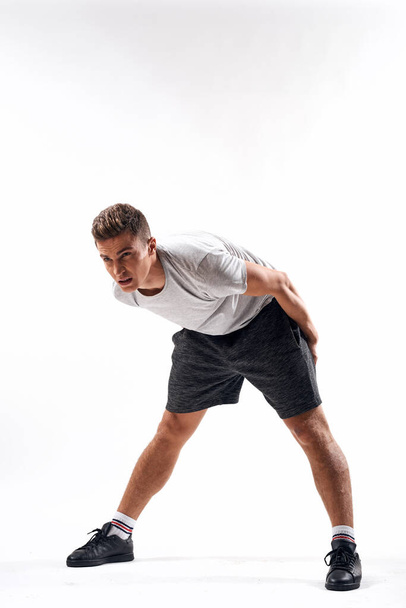 A sports man in shorts and a full-length T-shirt does exercises on a light background - Foto, immagini