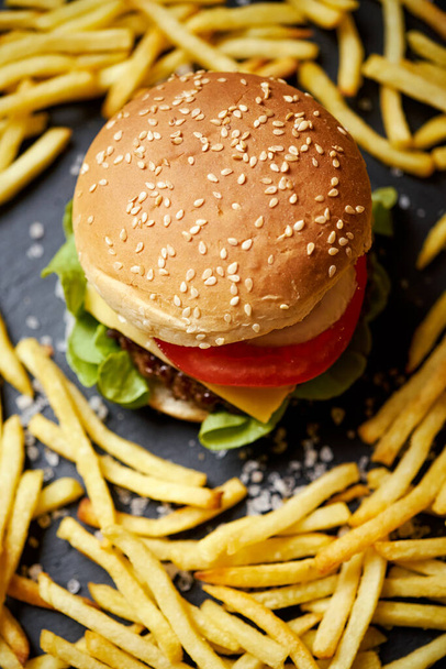 νόστιμο cheeseburger περιβάλλεται από τηγανητές πατάτες σε ένα μαύρο τραπέζι - Φωτογραφία, εικόνα