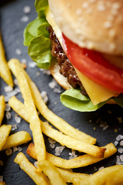 delicious cheeseburger surrounded by french fries on a black table - Foto, imagen