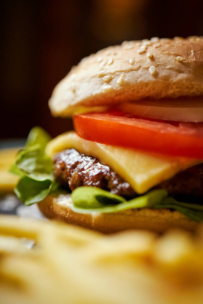 νόστιμο cheeseburger περιβάλλεται από τηγανητές πατάτες σε ένα μαύρο τραπέζι - Φωτογραφία, εικόνα
