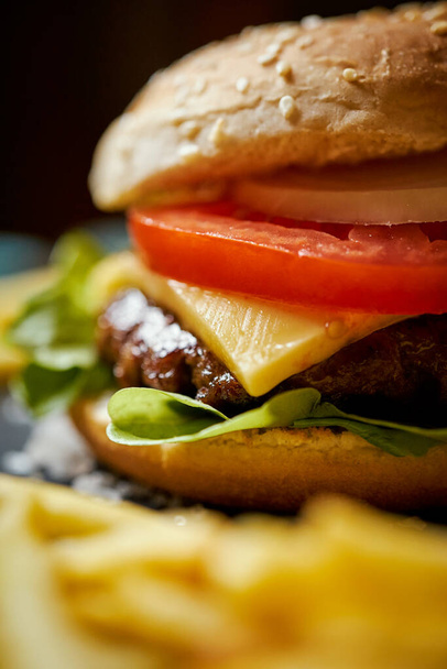 pyszny cheeseburger otoczony frytkami na czarnym stole - Zdjęcie, obraz