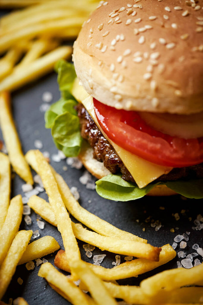 вкусный чизбургер в окружении картошки фри на черном столе - Фото, изображение