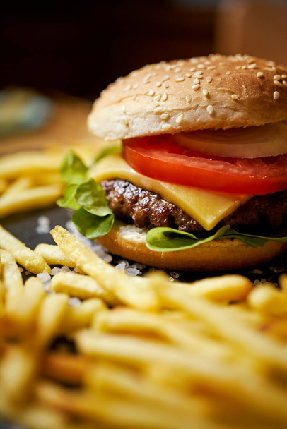 deliciosa hamburguesa con queso rodeada de papas fritas en una mesa negra - Foto, imagen