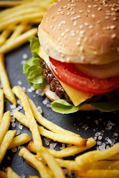 pyszny cheeseburger otoczony frytkami na czarnym stole - Zdjęcie, obraz