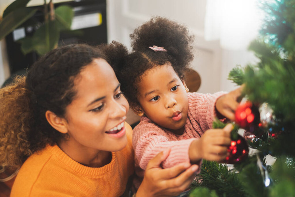 zwart afrikaanse moeder en haar schattige dochter versieren kerstboom voor kerst en gelukkig nieuw concept - Foto, afbeelding