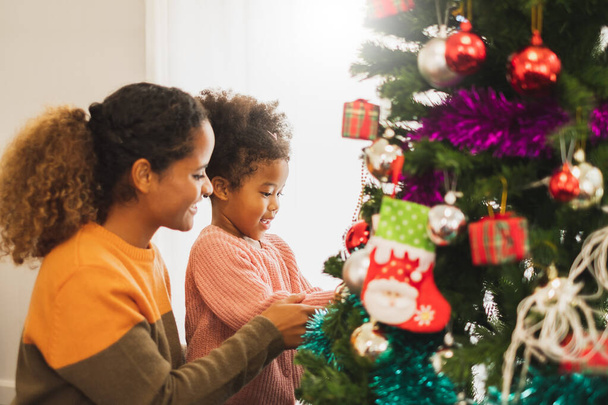 Black african mother and her cute daughter decorating christmas tree for christmas and happy new concept - Photo, Image