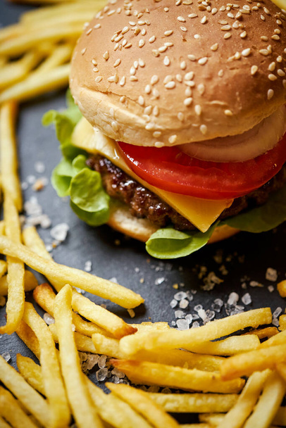 vynikající cheeseburger obklopený hranolky na černém stole - Fotografie, Obrázek