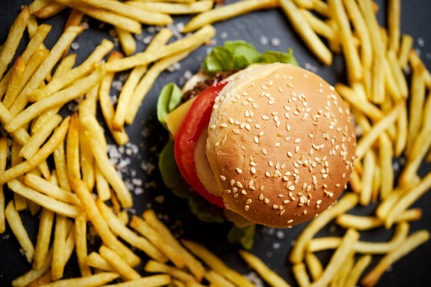 delicious cheeseburger surrounded by french fries on a black table - Photo, Image