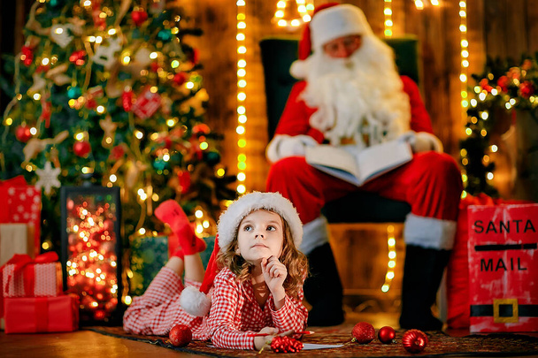 Merry Christmas, santa claus and little child girl at night at the Christmas tree - Fotografie, Obrázek