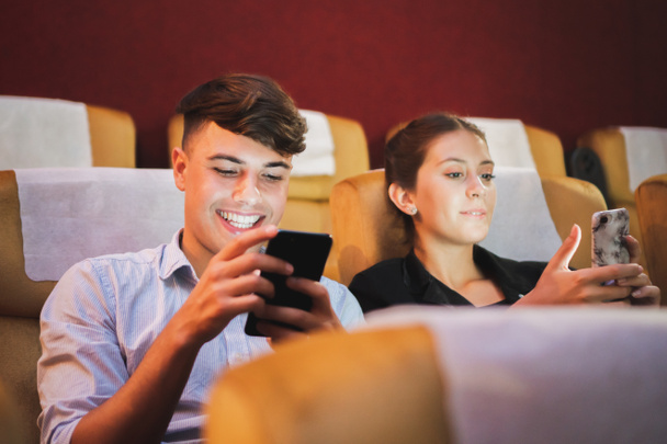 Young couple using phone in theatre/theater cinema while watching movie - Фото, зображення