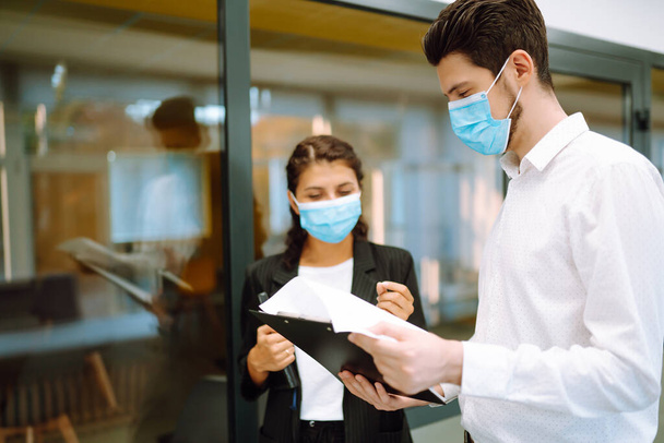 Business colleagues wearing medical face mask discussing together work issues at office. Teamwork during pandemic in quarantine city. Covid-19. - Φωτογραφία, εικόνα