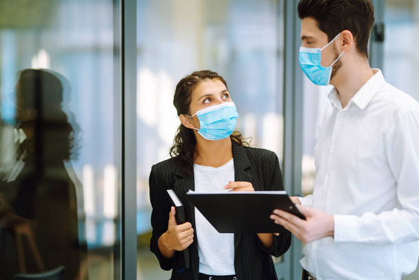 Business colleagues wearing medical face mask discussing together work issues at office. Teamwork during pandemic in quarantine city. Covid-19. - Фото, зображення