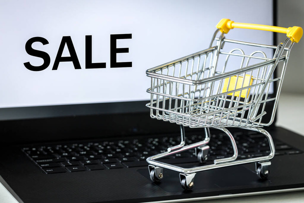 shopping cart on laptop keyboard. Monitor screen with the word SALE. The concept of online shopping and sales in online stores - Фото, зображення
