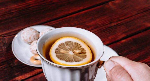 Tenez une tasse de thé avec du citron à la main. Tea party avec une délicieuse nourriture et des bonbons. Coffret tasse et thé blanc en céramique. - Photo, image