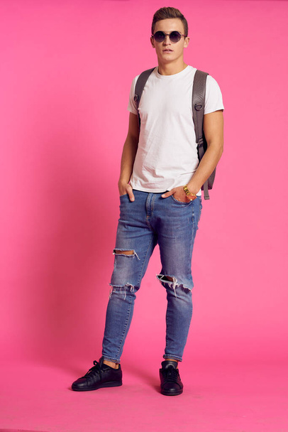 Portrait of a man in a white T-shirt and with a backpack on his back sunglasses pink background model - Foto, Bild