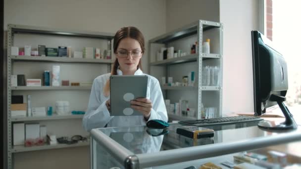 Έξυπνο κορίτσι φαρμακοποιοί σε γυαλιά με ένα ηλεκτρονικό δισκίο σε ένα φαρμακείο. - Πλάνα, βίντεο