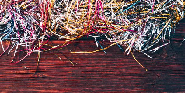 New year's multicolored shiny rain on a brown wooden table. Christmas decorations, bright colored tinsel. Beautiful Christmas wooden background in horizontal format. - Fotó, kép