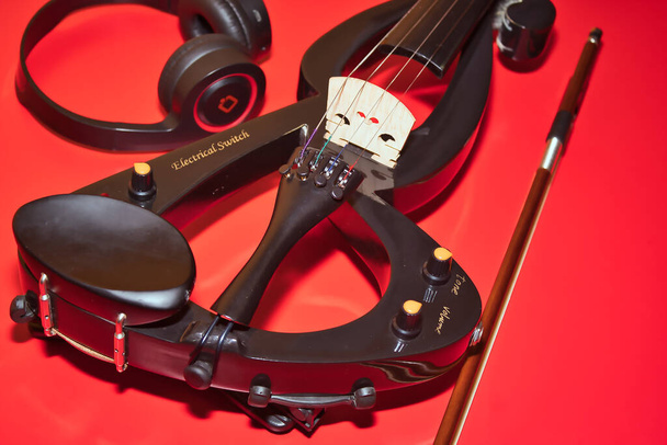 Detail elektrische Geige mit Bogen und Kopfhörer auf rotem Hintergrund und in horizontaler Position. - Foto, Bild