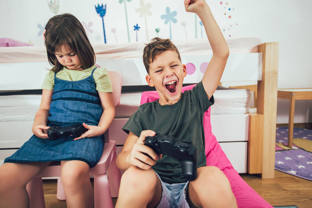 Pretty little girl and boy are playing game console and laughing at home - Фото, зображення