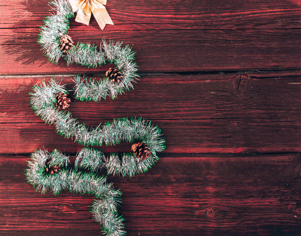 Glanzend groen tinsel in de vorm van een kerstboom met kegels en een gouden strik bovenop een houten ondergrond. Mooie kerstachtergrond. Gelukkig nieuwjaar en vrolijk kerstfeest. - Foto, afbeelding