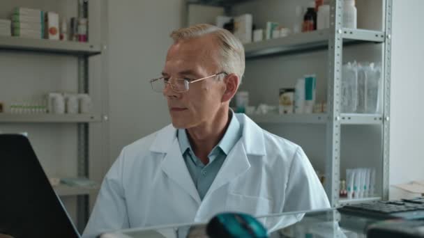 Érett orvos gyógyszerész fehér köpenyben és szemüvegben néz egy szöveges tabletta - Felvétel, videó