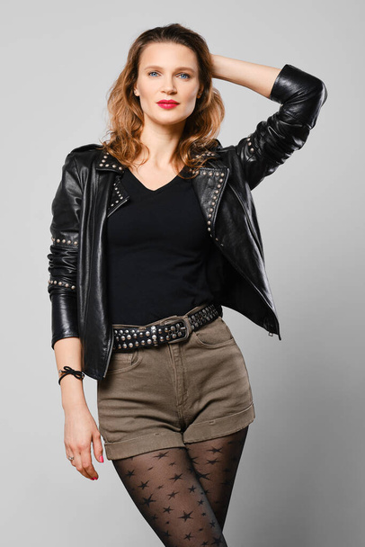 Studio portrait of trendy woman in leather jacket and shorts with natural make up and red lips - Foto, immagini