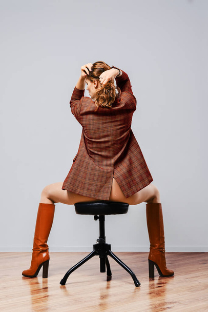 Back view of a woman in plaid jacket, white polka dot tights and leather knee boots sitting on chair - Фото, зображення