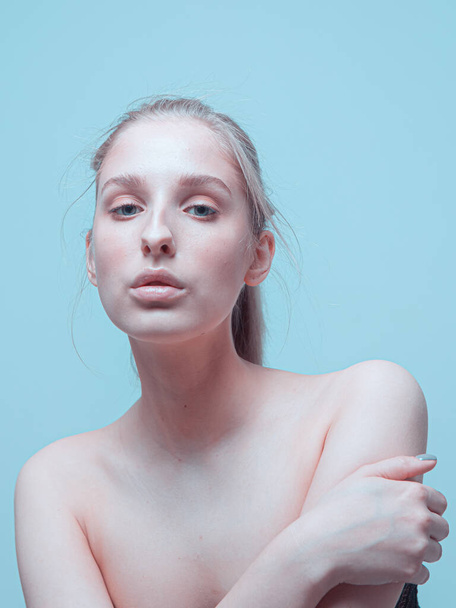 Close up portrait of young pretty girl with naked shoulders, perfect skin and gentle make up on blue studio background - Фото, изображение