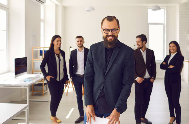 Cheerful young businessman with group of employees smiling and looking at camera - Valokuva, kuva