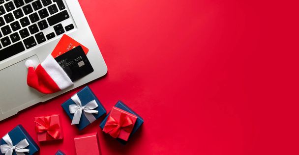 on a red banner background lie a computer laptop laptop bank credit cards in a santa hat and gifts in boxes with bows of red and blue colors  - 写真・画像