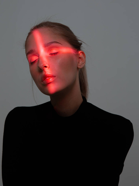 Portrait of young pretty girl with cross shaped red light on her face and closed eyes - Fotografie, Obrázek
