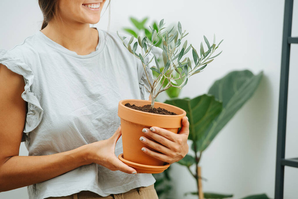 Smiling young woman holding potted plant in hands. Cropped, half of the face - Foto, Imagen