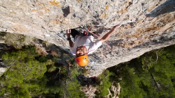 Man leiden klimmen in de natuur rots en cliping de volgende quickdraw, aan zee, in Andratx kustlijn, Mallorca eiland, Spanje.Low angle, twist beweging, 4K 60p. - Video