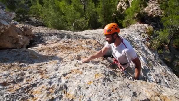 Man leiden klimmen in de natuur rots en cliping de volgende quickdraw, aan zee, in Andratx kustlijn, Mallorca eiland, Spanje.Low angle, twist beweging, 4K 60p. - Video