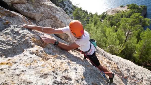 男は自然の岩の中で登山をリードし、海の横に、アンドラックス海岸線、マヨルカ島、スペインの次の速攻をクリップします。低角度、ねじれ運動、 4K 60p. - 映像、動画