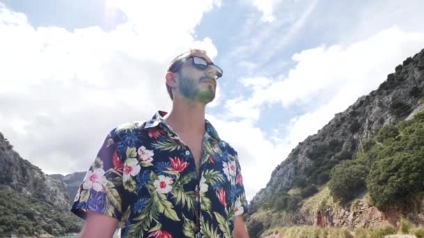 Man modellering met Hawaïaanse shirt en zonnebril in prachtige zonnige dag met berglandschap in de rug, Gorg blau uitkijk, Mallorca eiland, Spanje.Hoge hoek, reizen + parallax bewegingen, slow motion, HD. - Video