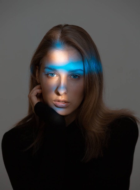 Creative portrait of stylish young woman with blue neon light on face and perfect skin on gray background - Foto, immagini