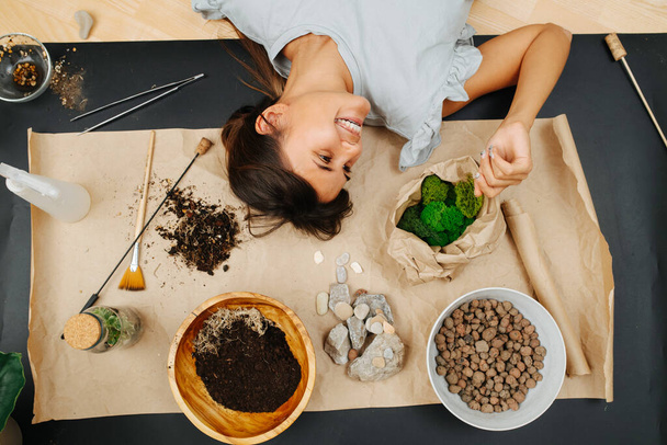 Happy woman lying on a mat on the floor with indoor gardening theme items. - Фото, зображення