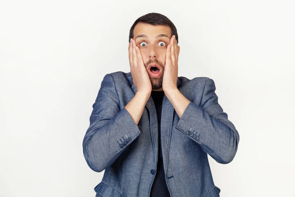 Young businessman man with a beard scared and shocked, surprised and surprised with hands on his face. Portrait of a man on a gray background. - Foto, Imagen